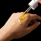 Hand applying yellow liquid from a dropper onto skin against a black background