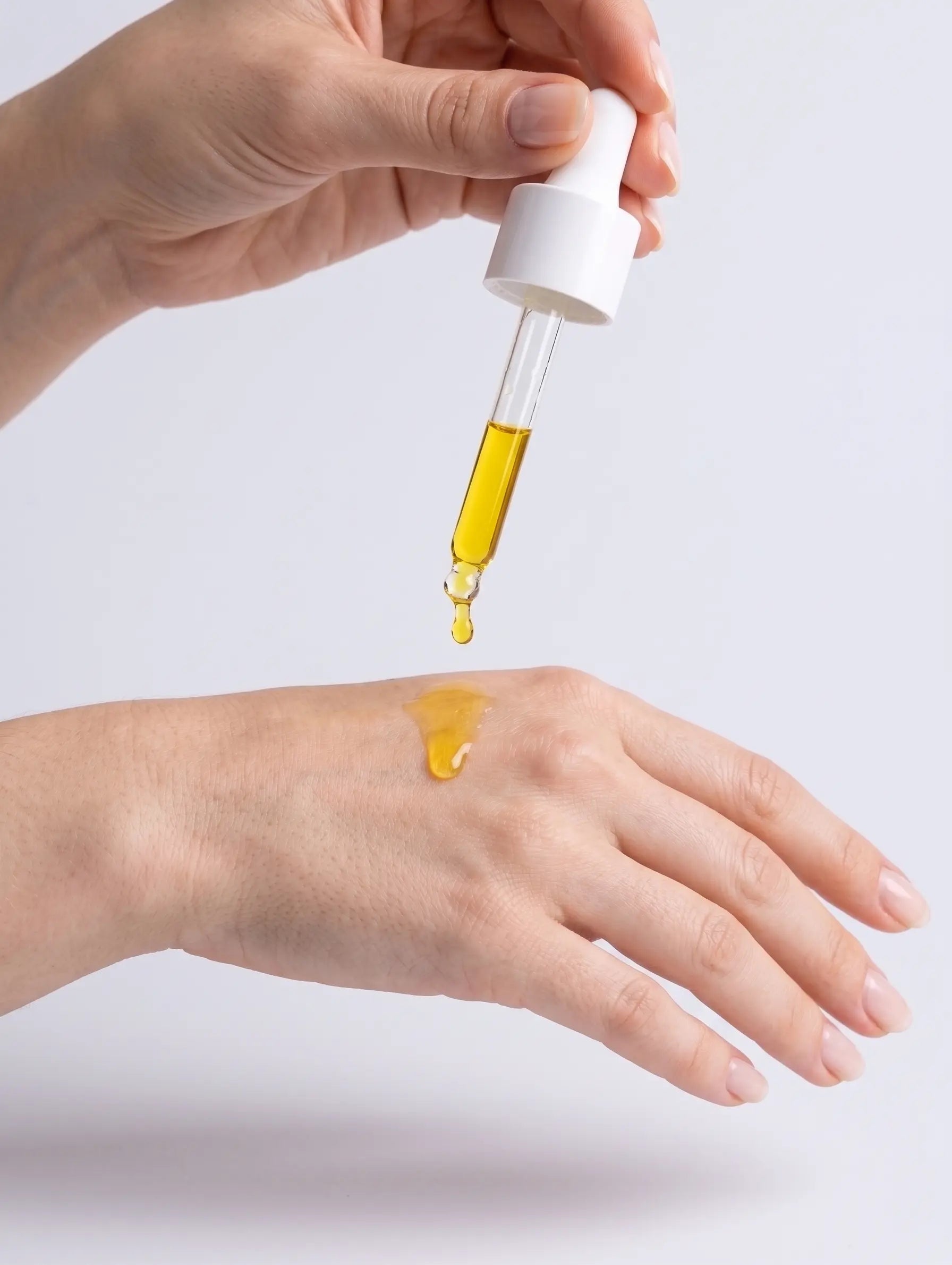 Applying Sirela Bio-Retinol Bakuchiol Concentrate — golden bakuchiol serum dispensed from a glass dropper onto the back of the hand