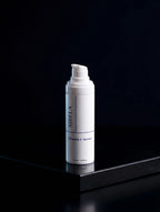 A white cylindrical pump bottle of SIRELA Vitamin C Serum standing upright on a glossy black surface against a very dark black background.