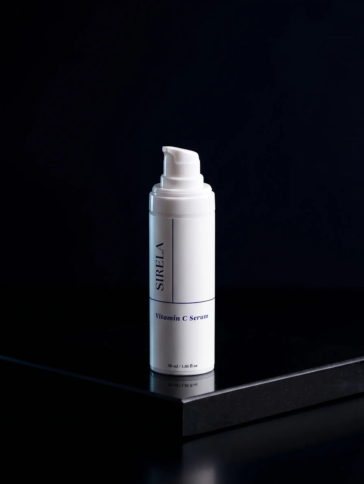A white cylindrical pump bottle of SIRELA Vitamin C Serum standing upright on a glossy black surface against a very dark black background.